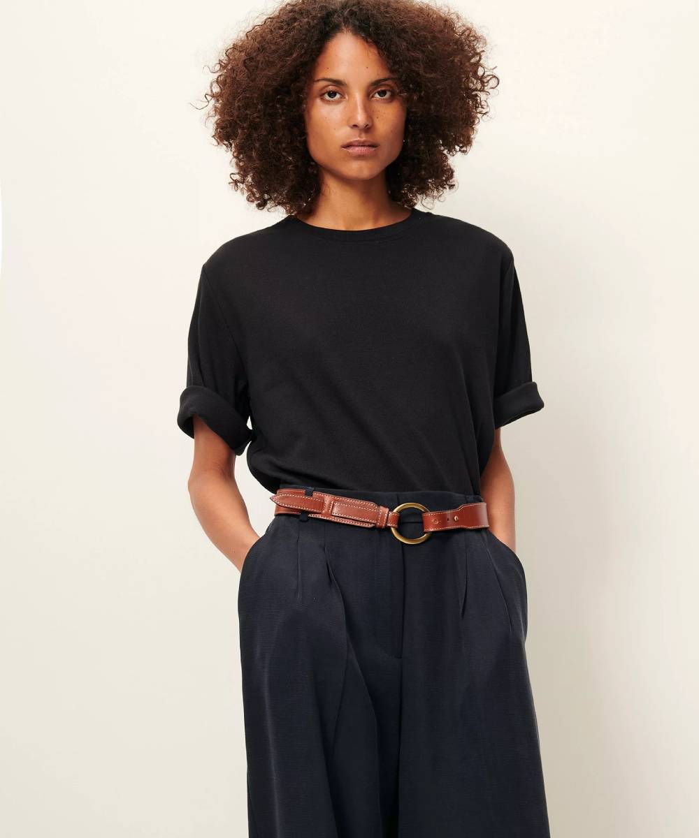 Mujer llevando una camiseta negra, acanalada, con mangas holgadas y con dobladillo. Pantalón en el mismo tono y cinturón en color cuero. La Folie Santander.