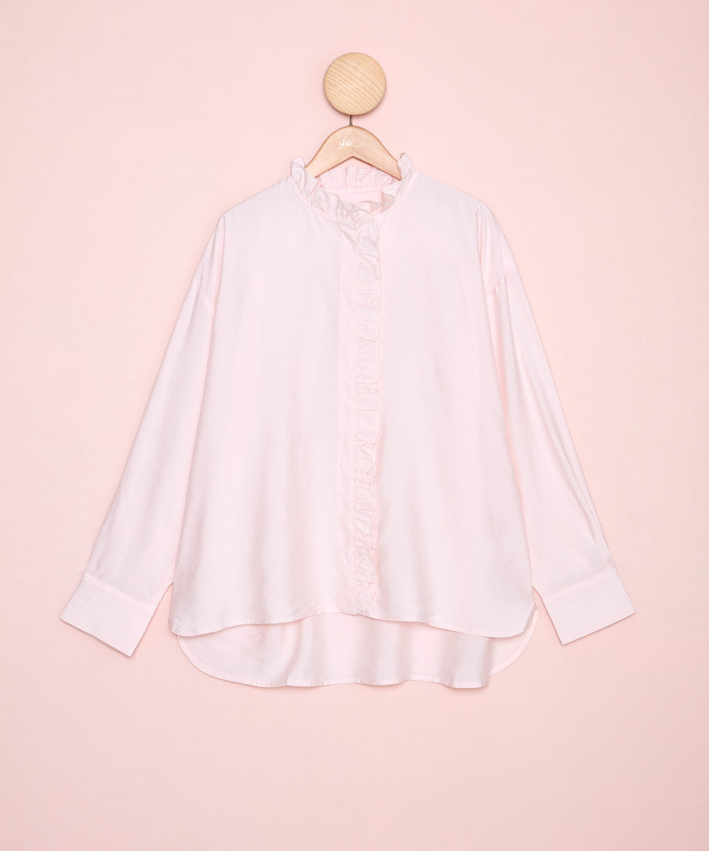 Vista frontal de una camisa en color rosa con el cuello redondo y volante festoneado. Cierre con botonadura bajo tapeta. La Folie Santander.